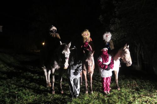 At night, three people on horses in wigs and beard, one in blackface, and two people standing between them.