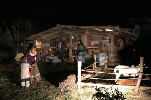 At night, a family gathers in an outdoor home scene, with a pen of goats to the right.
