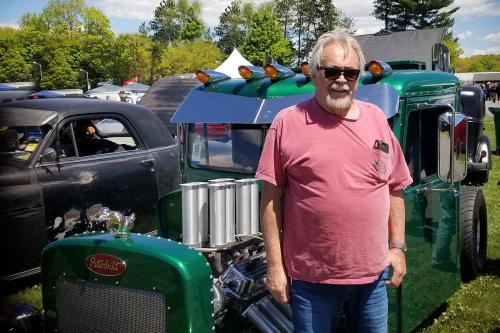 A man poses next to a green antique car. 