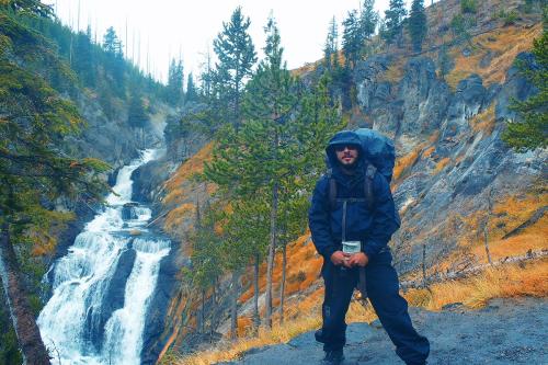 Jiménez poses besides a waterfall, surrounded by orange brush and green pine trees.
