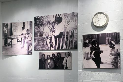 Four black-and-white photographs of Black adults and children on a white wall, along with a clock.