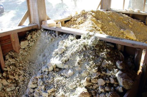 Two piles of dried chunky clay in an open-air enclosure. One pile is more yellow, the other grayish-blue.