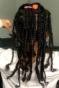 From behind, a young girl with long braid holds up her fists, as if to show off bicep muscles.