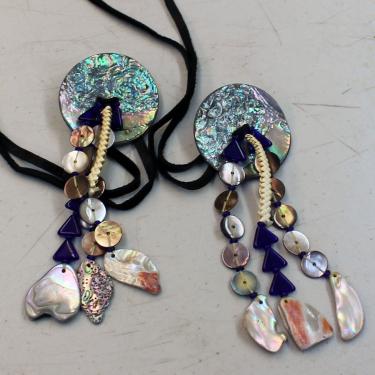 Close up on two pieces of jewelry, each made of small pieces of irridescent shell strung together and fixed to long black cords.