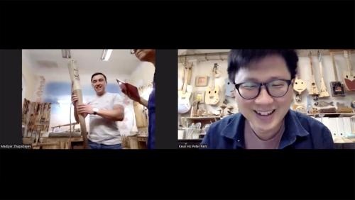 Screenshot from Zoom meeting with two people: Madiyar Zhapabayev on the left, holding a wooden staff in a woodworking studio, and Keun Ho Peter Park on the right, with several wooden guitar-like instruments on the wall behind him.