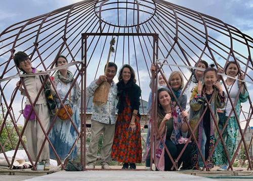 Ten people pose inside the criss-crossed frame of a dome-shaped yurt, smiling. 