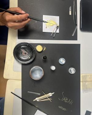 From above, a table is set with black paper placemats, small containers, Q-tips, brushes, and small ceramic bowls.