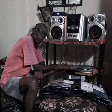 A man sits in front of a silver stereo and book full of CDs.