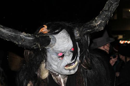 A person in a Krampus costume with blueish skin, glowing red eyes, and wide black horns.