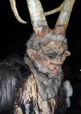 A person in a Krampus costume with tall, thick horns and gray fur on its head and neck.
