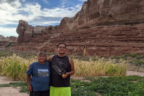 A mother and grown son pose, arms around each other, by their melon patch, cliffs rising in the background.