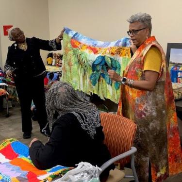 Two women hold up a colorful quilt with a pattern of palm trees.