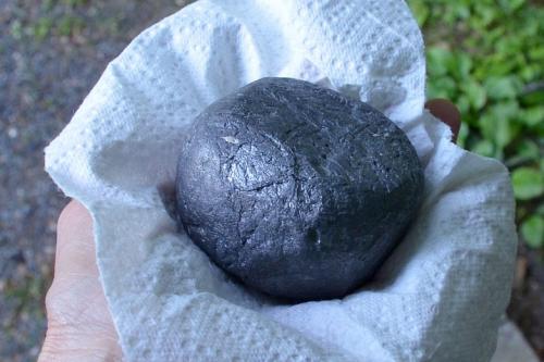 Closeup on a hand holding a ball of molten gray metal, about the size of a tennis ball, in a white paper towel.