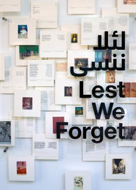 An exhibition display with the Arabic and English title: Lest We Forget in black letters on glass. Behind it, several pages of a book with text and photos mounted on a white wall.