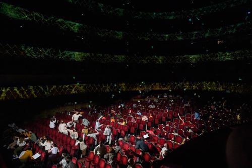 View of audience and performers in the red seats of an opera hall, a view from the stage.