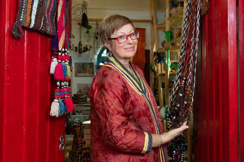 A woman poses in a double-doorway, with embroidered textiles hanging on the open doors.