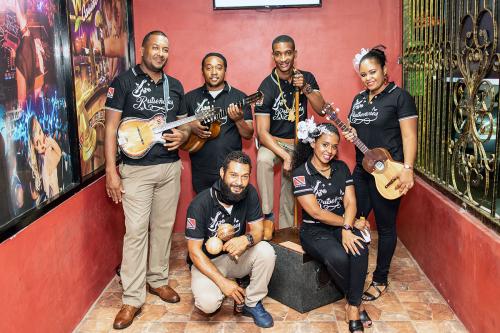 Six band members pose holding their instruments: small guitar-like instruments, maracas, and other percussion.