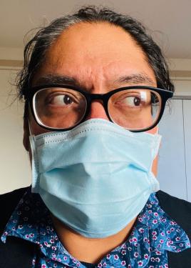 Selfie of a man in glasses, disposable mask, and blue collared shirt.