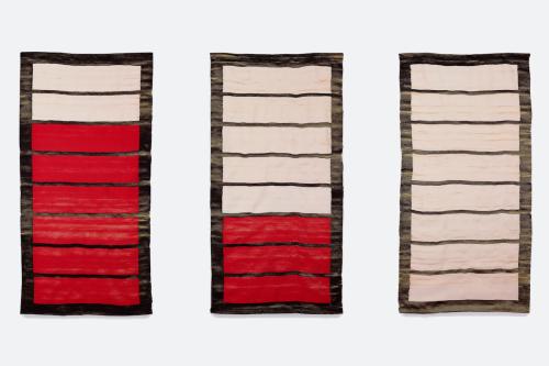 Art piece of three woven designs hanging on a wall. Each is a rectangle subdivided into eight parts. In the box on the left, six of the eight parts are red, the others white. In the middle, three parts are red. On the right, all parts are white.
