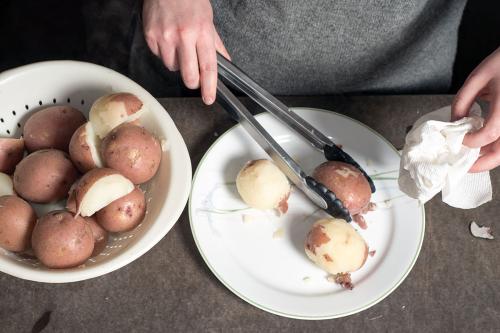 Closeup of author’s hands working on removing skins from boiled potatoes.
