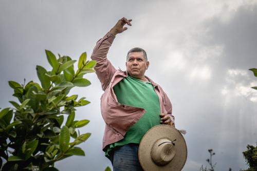 A man with green shirt and pink overshirt, wide-brimmed hat in hand, throws one up toward the gray sky.