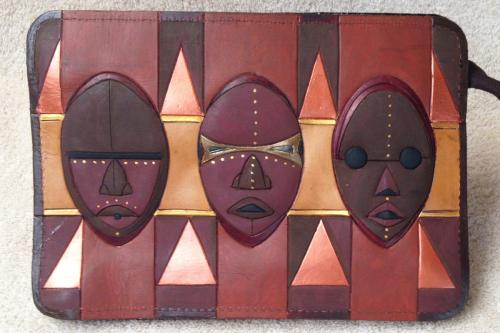Rectangular brown leather wallet, with a design of three African masks on a geometric shape background. 