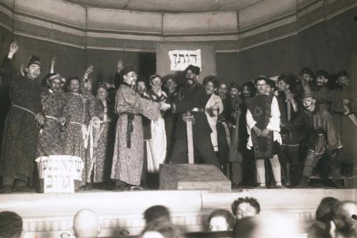Cast of a play, looks like all men, gather and wave on stage. Black-and-white archival photo.