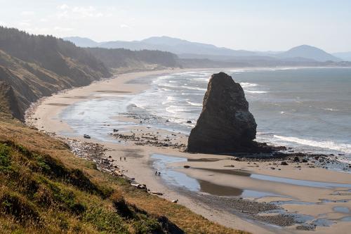 Along a curving coastline, a large boulder protrudes from the beach.