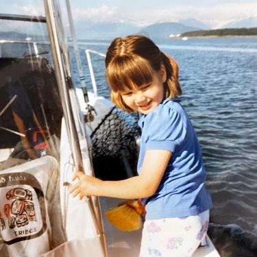 A young girl on a boat at sea, smiling as she looks over her left shoulder.