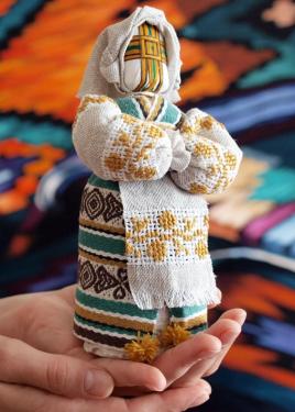 Close-up on a hand holding upright a doll with embroidered dress and apron, and an embroidered cross in place of a face.