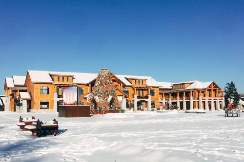 Under a clear blue sky, in a clearing covered in snow, stands a three-story yellow building and a large, pyramid-shaped sculpture.