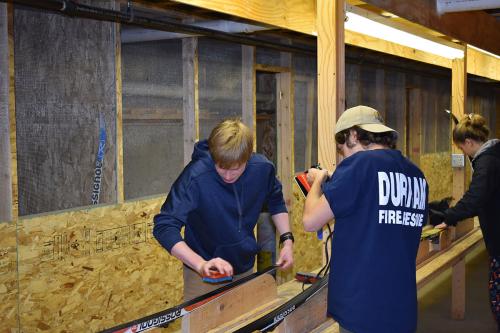 Three people work on a set of skis indoors.