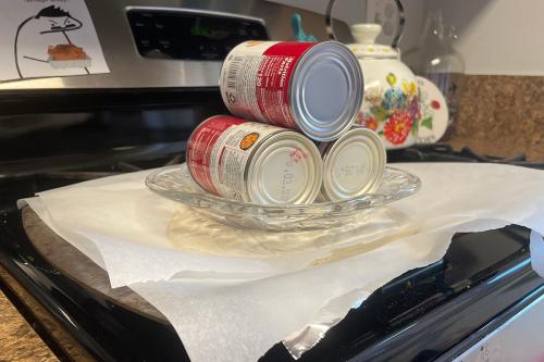 On a stovetop, three soup cans are stacked on a glass plate, which rests on top of layers of parchment paper, with a pale circle of dough peaking out from between the layers.