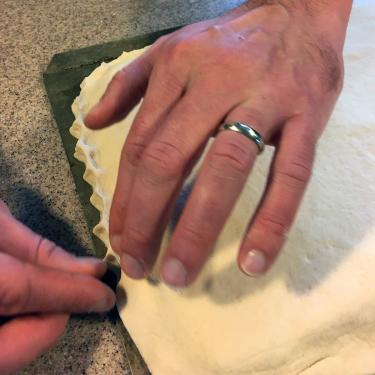 Close-up on a pair of hands crimping the edge of a rectangular slab of bread.
