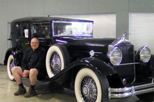 A man sits on the side step of a black antique car.