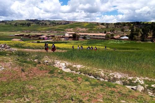 Wide shot of a green landscape with people walking uphill, billowy clouds in the background.