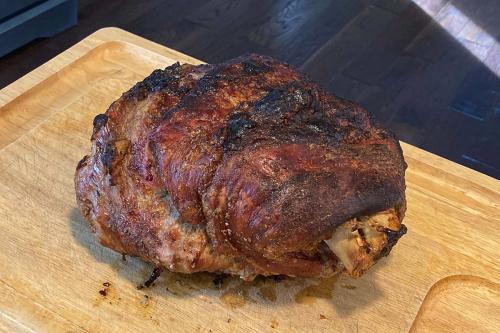 A large piece of raosted meat on a cutting board, bone in, skin crispy and blackened on top.
