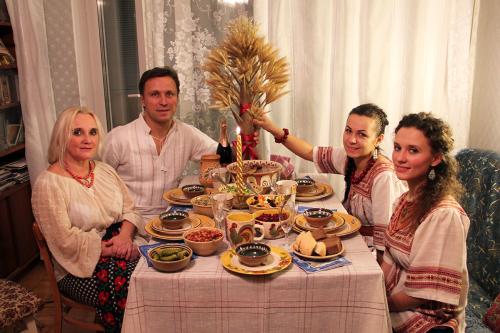 A family of four poses, seated at a decorated dinner table with several dishes, a lit candle, and a centerpiece resembling a stalky tree tied with red ribbon.