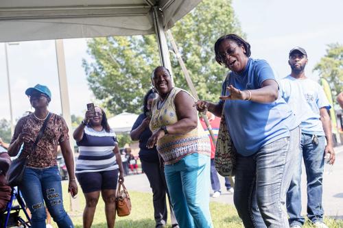 Women dance under a tent outdoors while others stand and watch or record on their phones.