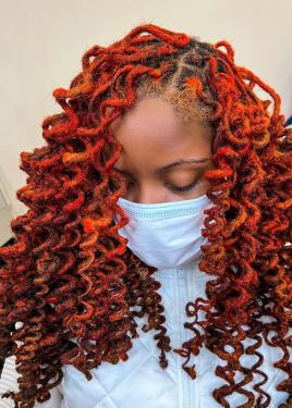 A person with eyes closed, face mask on, with bright red curled dreadlocks.