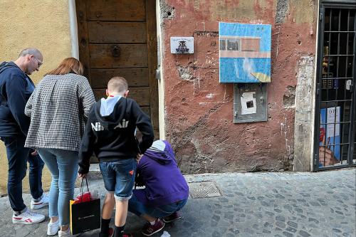 A family of four stops on a cobblestone street, looking down at plaques.