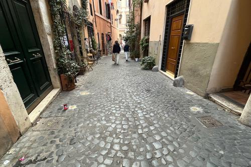 View down a narrow cobblestone street. In front of the doorways, small brass plaques are barely visible, laid in the street.
