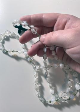 Closeup on a hand holding white and clear rosary beads.