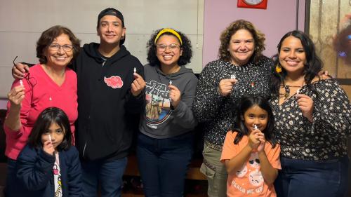 Seven adults and children pose arm in arm, each holding up a tiny white figurine.