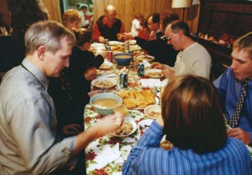 A family sits around a long table in a wood-paneled room. The table is full of plates of food.