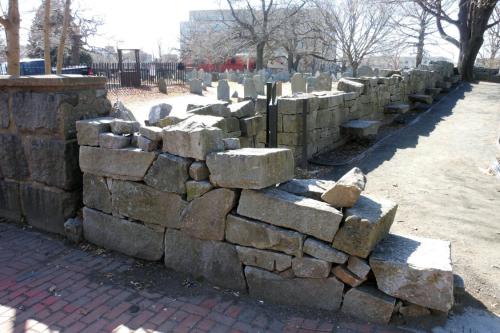 Corner of a low stone wall, bordering a graveyard. The stone have no mortar and are falling down.
