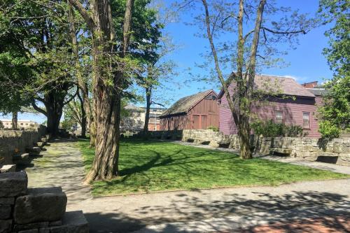 A grassy courtyard bordered by a low stone wall, red wooden buildings in the background.