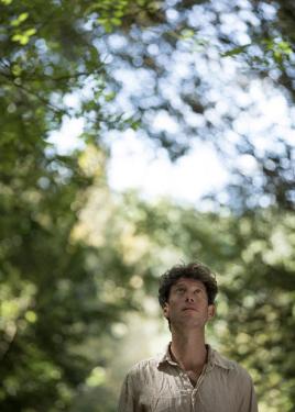 A man gazes upward at green trees.