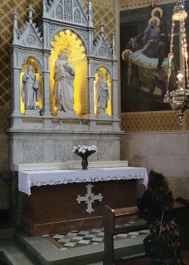 A person kneels in front of a church altar, with the Virgin Mary holding the baby Jesus illuminated.