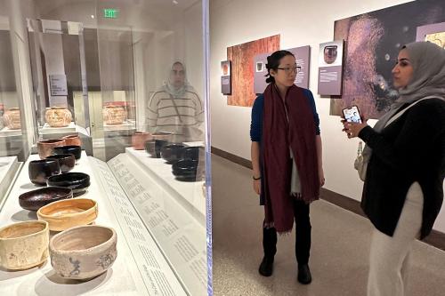 Three people stand in a museum gallery next to a display of ceramic bowls.